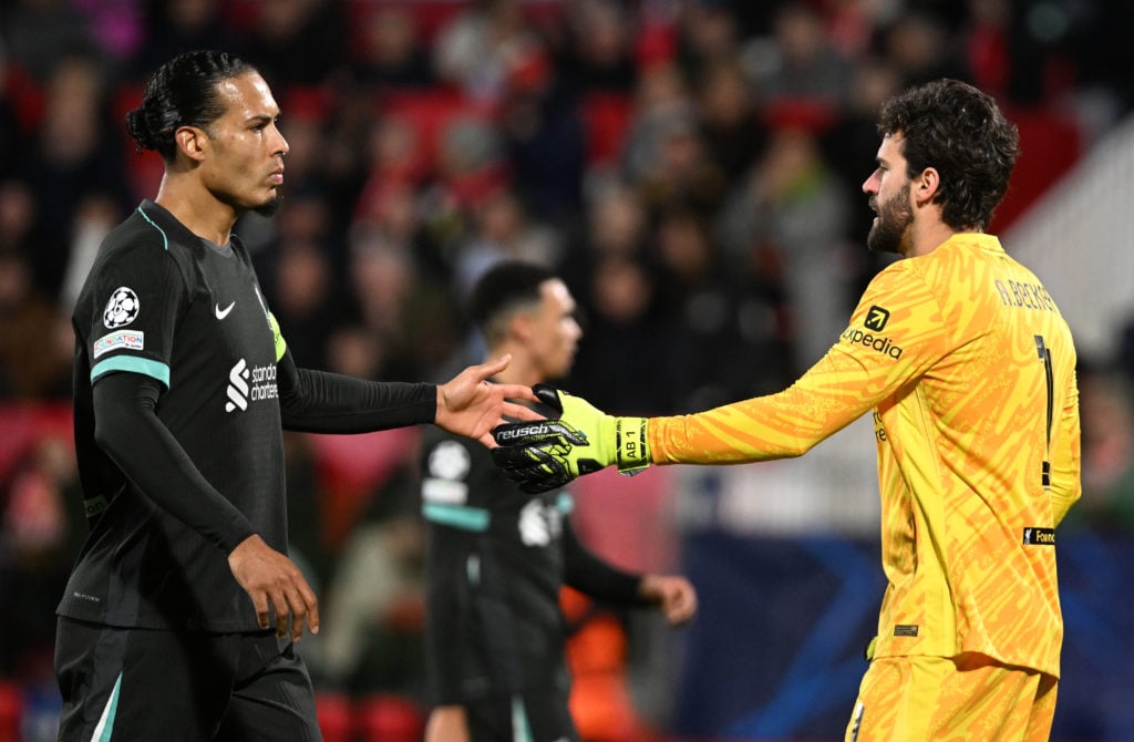 Virgil van Dijk and Alisson reaching out to hi-five one another in a Champions League clash for Liverpool.