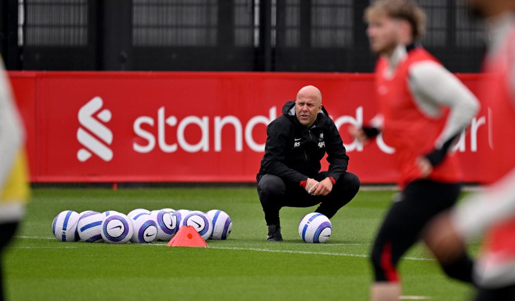Arne Slot crouches as he watches Liverpool players during a training session.